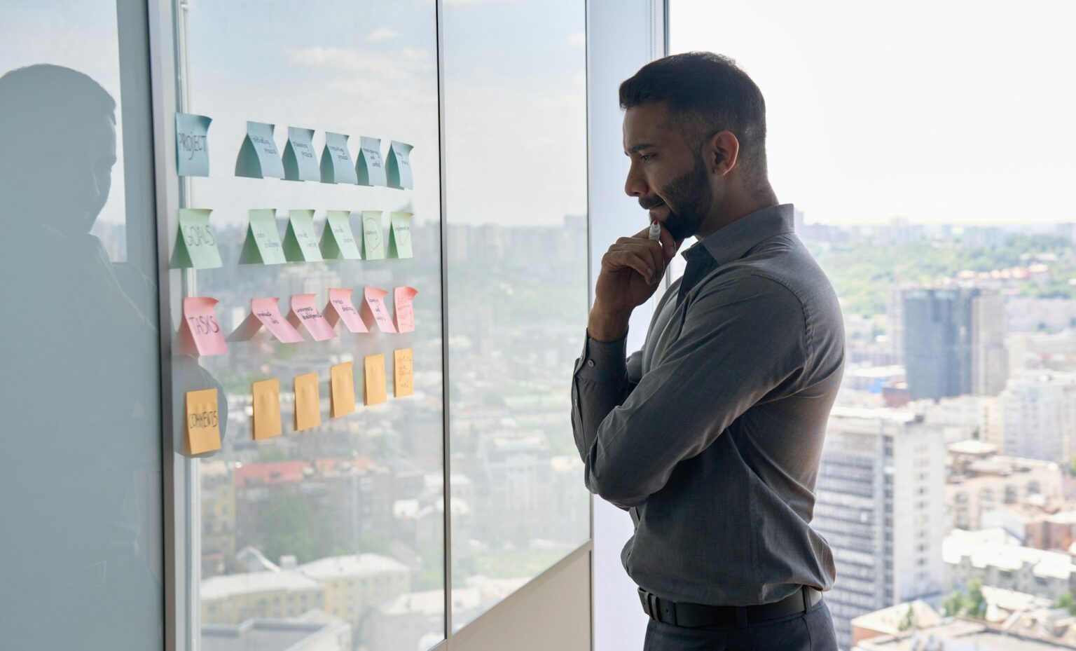Indian businessman thinking about project strategy at board with sticky notes.